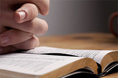 Picture of a person with their hands folded over a bible